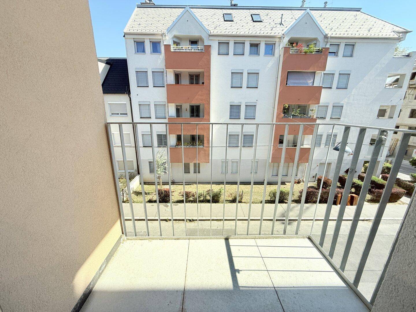 Kleiner Balkon mit Fliesenboden und Metallgeländer, bietet Blick auf den Innenhof der Wohnanlage.