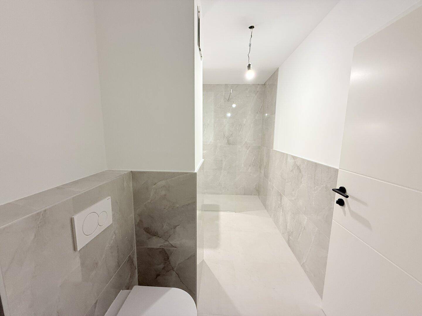 Modernes Gäste-WC mit grauen Fliesen, wandhängender Toilette und minimalistischem Design.