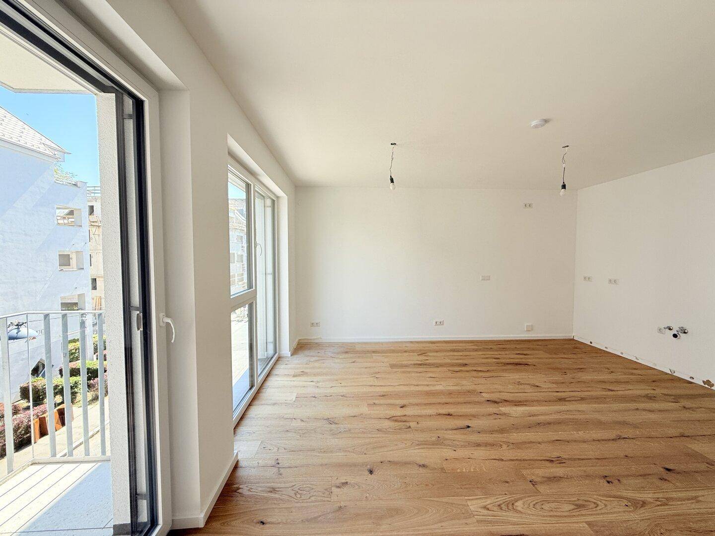 Lichtdurchfluteter Raum mit Holzboden und Zugang zu einem Balkon, ideal für offenes Wohnen.