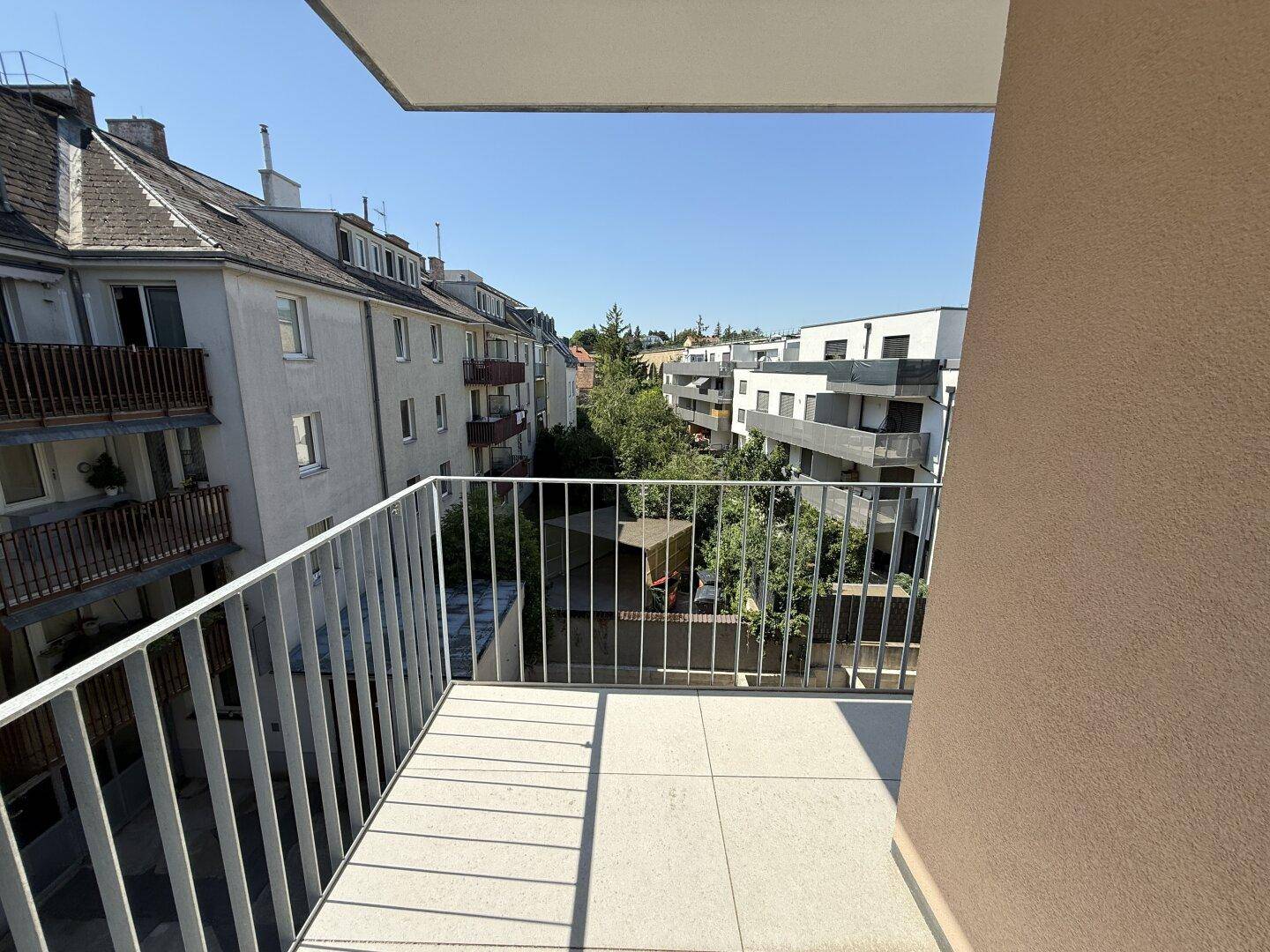 Heller Balkon mit Fliesenboden und Metallgeländer, bietet einen Blick auf die umliegenden Gebäude.
