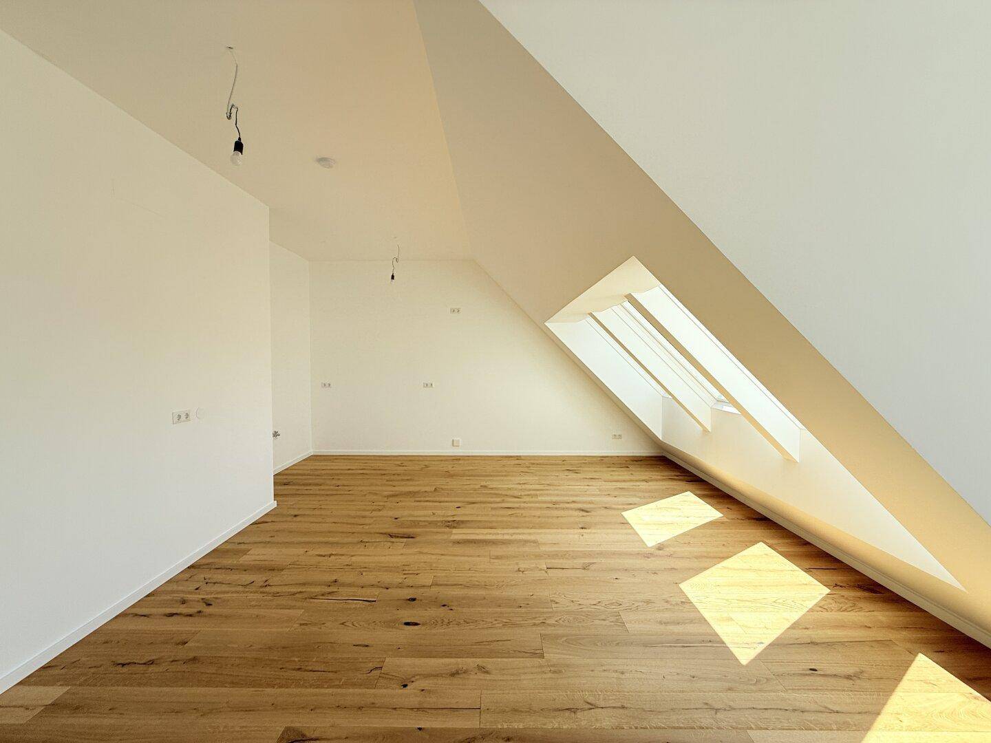 Geräumiges Dachgeschosszimmer mit schrägen Wänden und hellem Holzboden, ideal für Wohnzwecke und lichtdurchflutet.