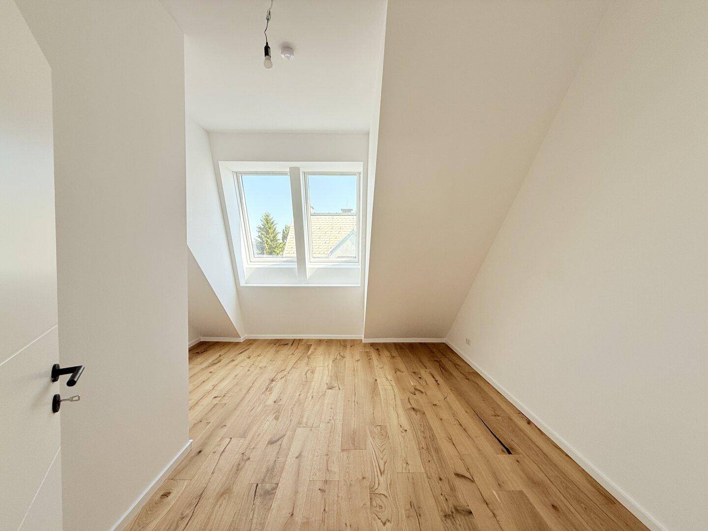 Helles Schlafzimmer im Dachgeschoss mit Holzboden und einem Fenster, das viel Licht hereinlässt.