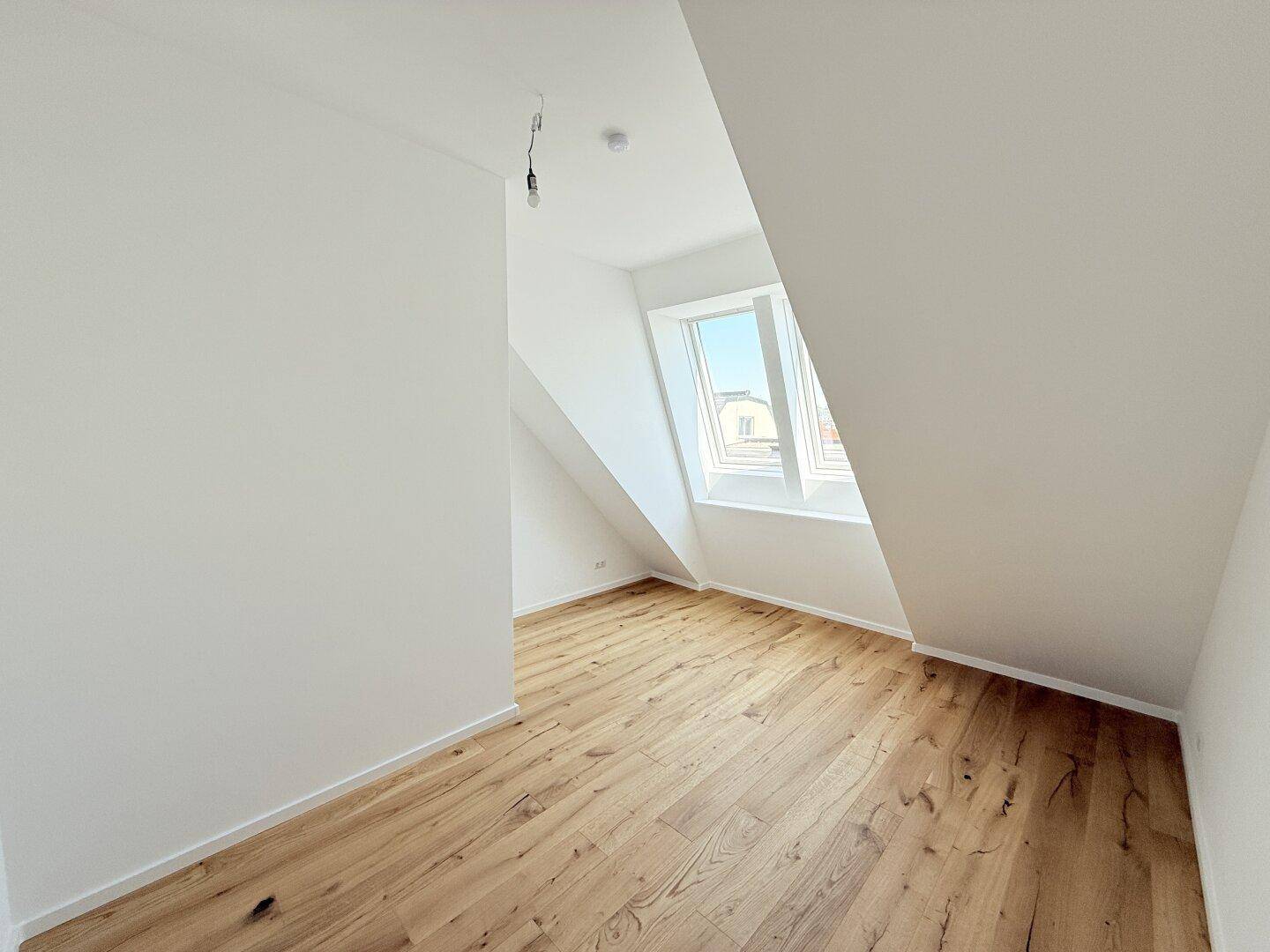 Geräumiges Dachzimmer mit Holzboden und schrägen Wänden, ideal als Schlaf- oder Arbeitszimmer nutzbar.