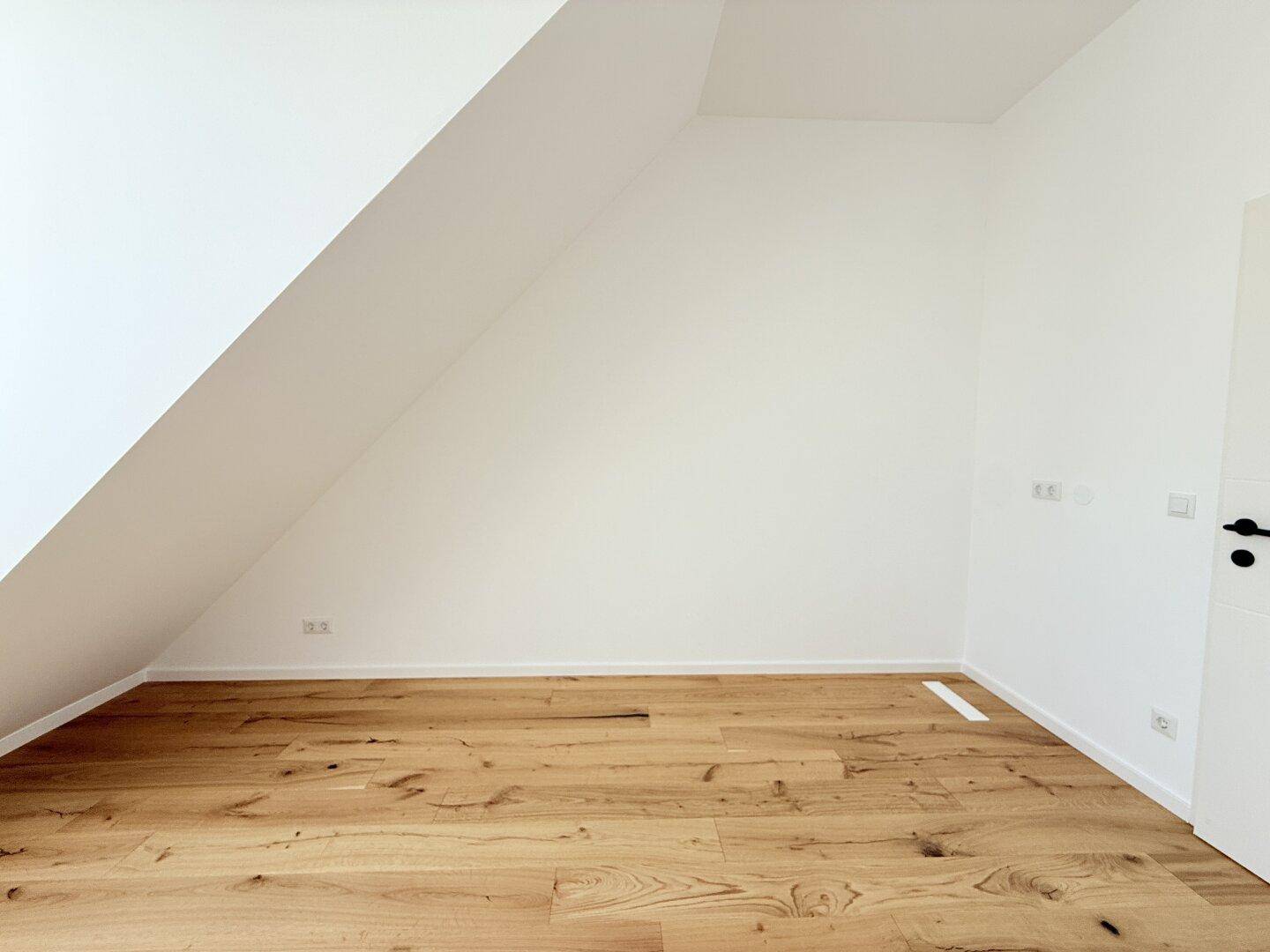 Leerer Raum im Dachgeschoss mit Holzboden und schräger Wand, vielseitig nutzbar und in gutem Zustand.
