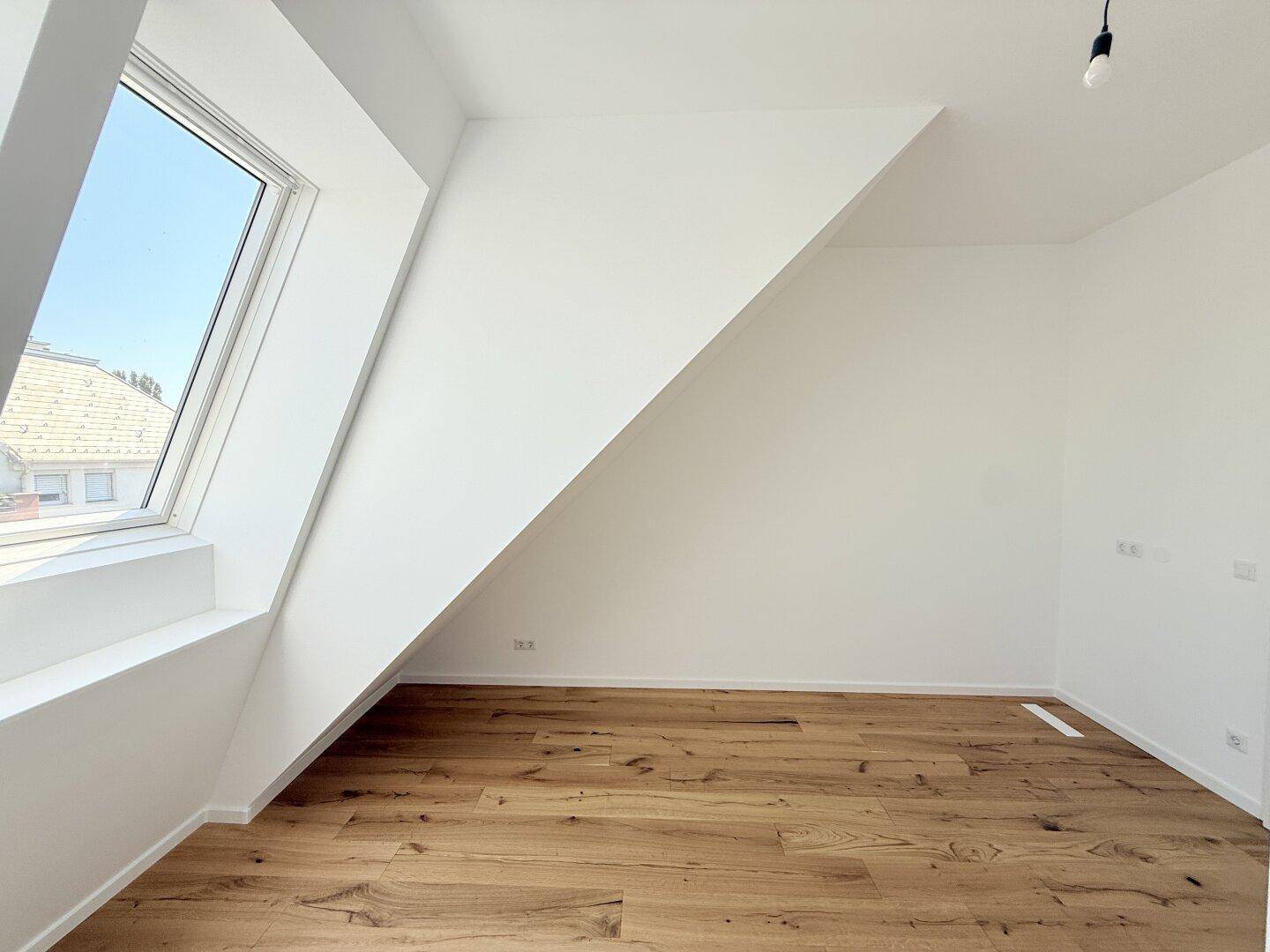 Heller Dachgeschossraum mit Holzboden und einem Dachfenster, das Tageslicht spendet und Ausblick bietet.