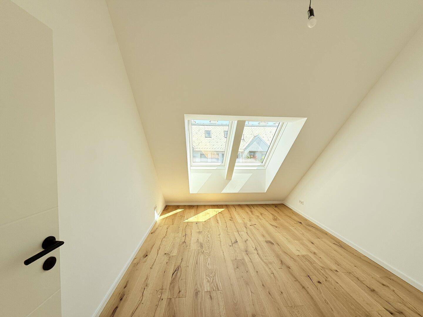 Geräumiges Dachgeschosszimmer mit Holzboden und zwei Dachfenstern, bietet viel Helligkeit und Ausblick.