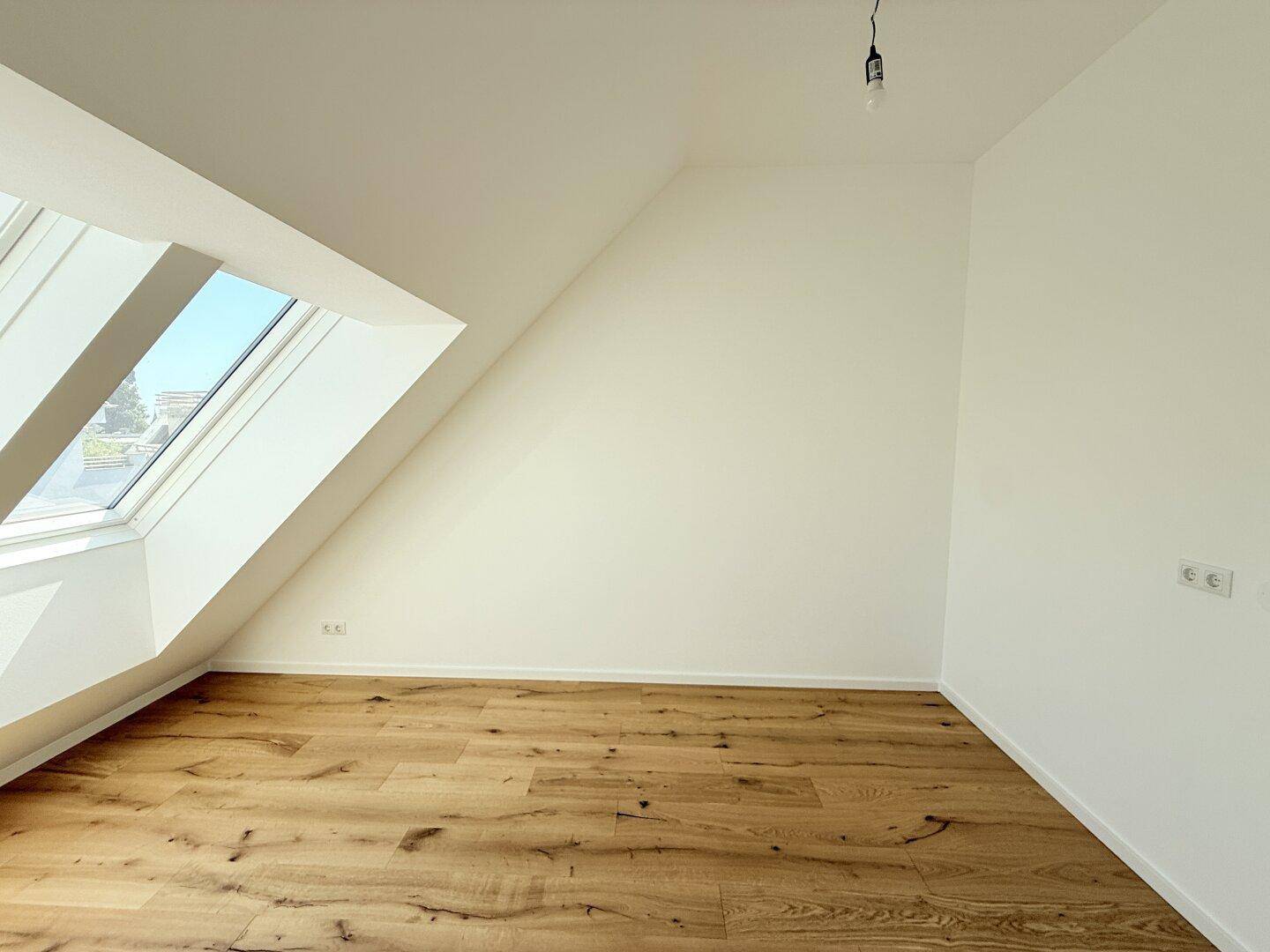 Heller Dachgeschossraum mit Holzboden und einem großen Dachfenster, ideal als Schlafzimmer nutzbar.
