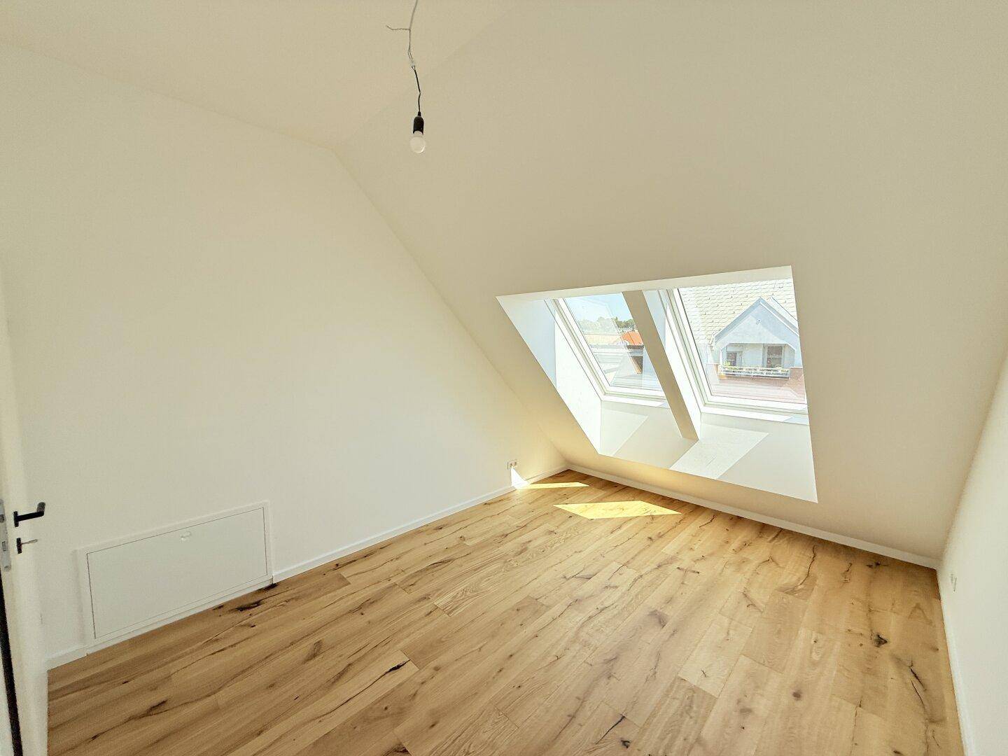 Lichtdurchflutetes Dachgeschosszimmer mit Holzboden und mehreren Dachfenstern, bietet weite Ausblicke.