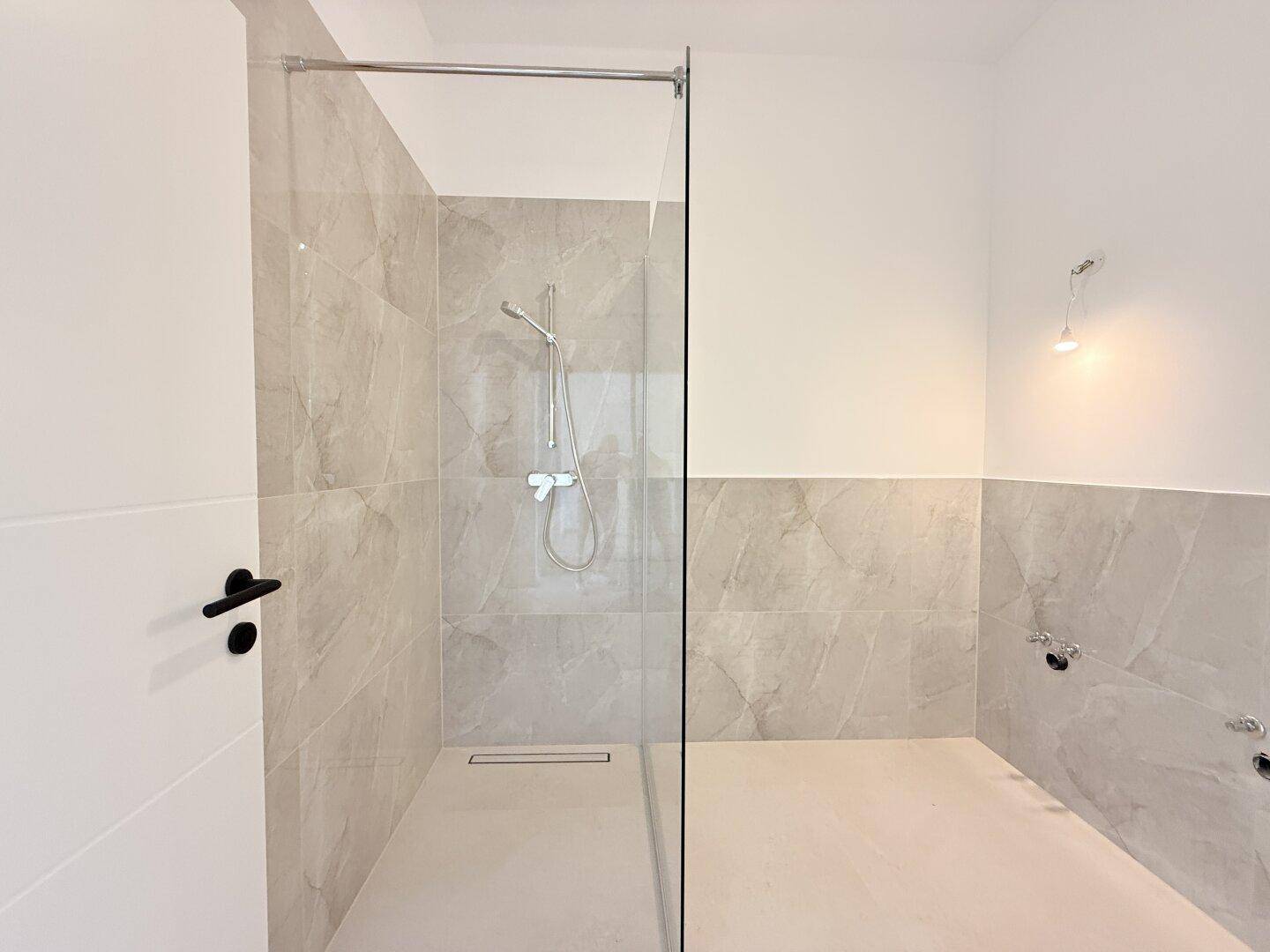 Helles Badezimmer mit großer begehbarer Dusche und modernen Fliesen, noch ohne Armaturen, sehr geräumig.