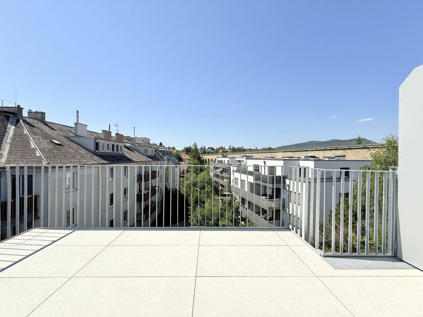 Große, geflieste Terrasse mit Metallgeländer und weitem Blick über die Stadt und grüne Umgebung.