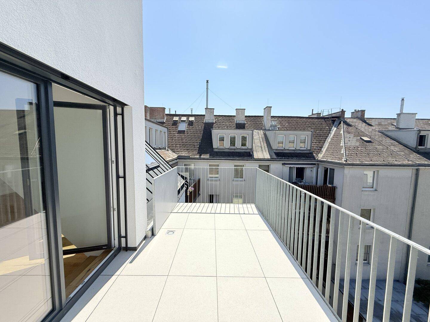 Heller Terrassenbereich mit Fliesenboden und Blick auf umliegende Dächer und Gebäude, ideal zum Entspannen.