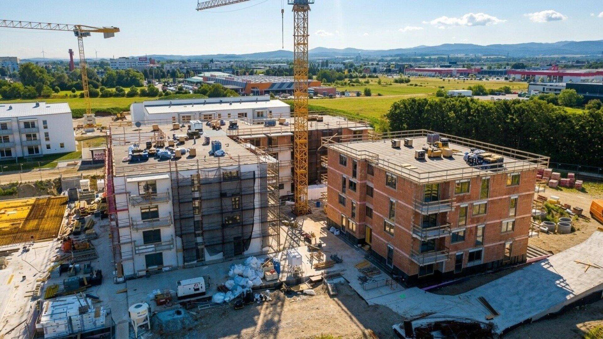 Luftaufnahme einer großen Baustelle mit mehreren im Bau befindlichen Gebäuden und Kränen unter blauem Himmel.