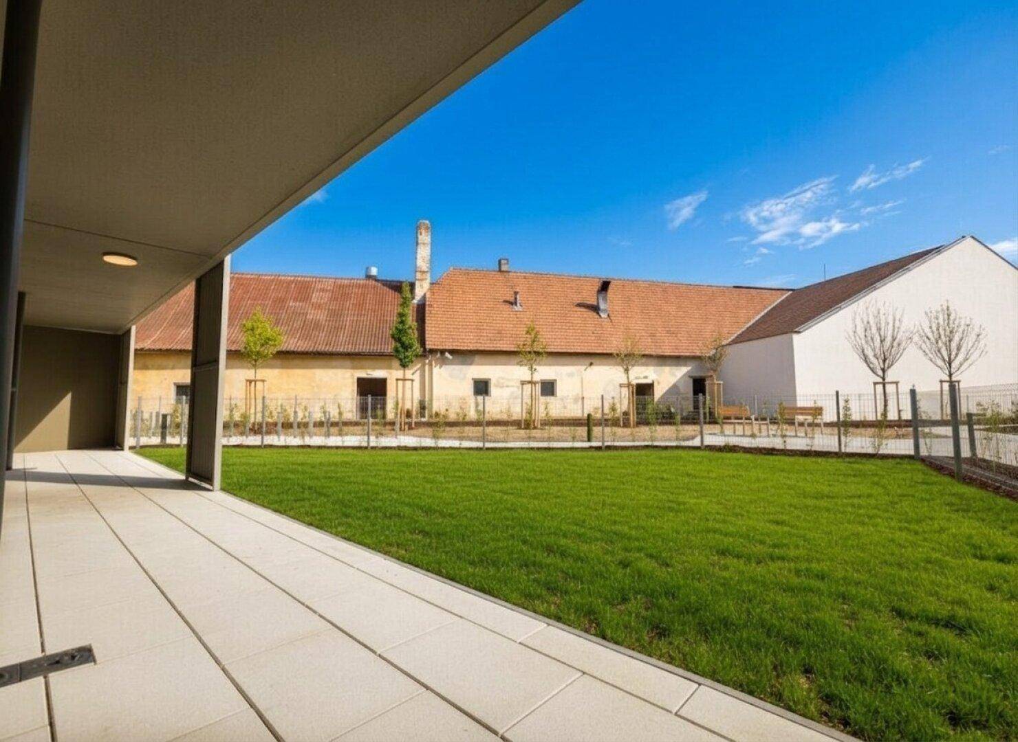 Weitläufige Terrasse mit Blick auf einen gepflegten Rasen und historische Gebäude im Hintergrund.
