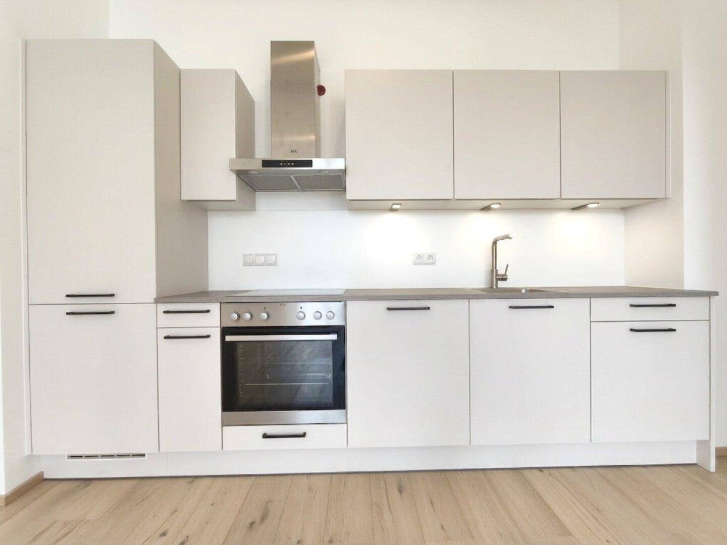 Moderne Einbauküche in Grau mit Edelstahlofen und Dunstabzugshaube.