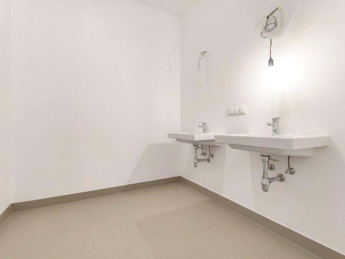 Unmöbliertes Badezimmer mit zwei Waschbecken und hellen Fliesen.