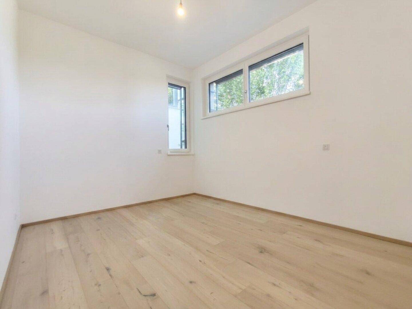 Helles Schlafzimmer mit Holzboden und zwei Fenstern.