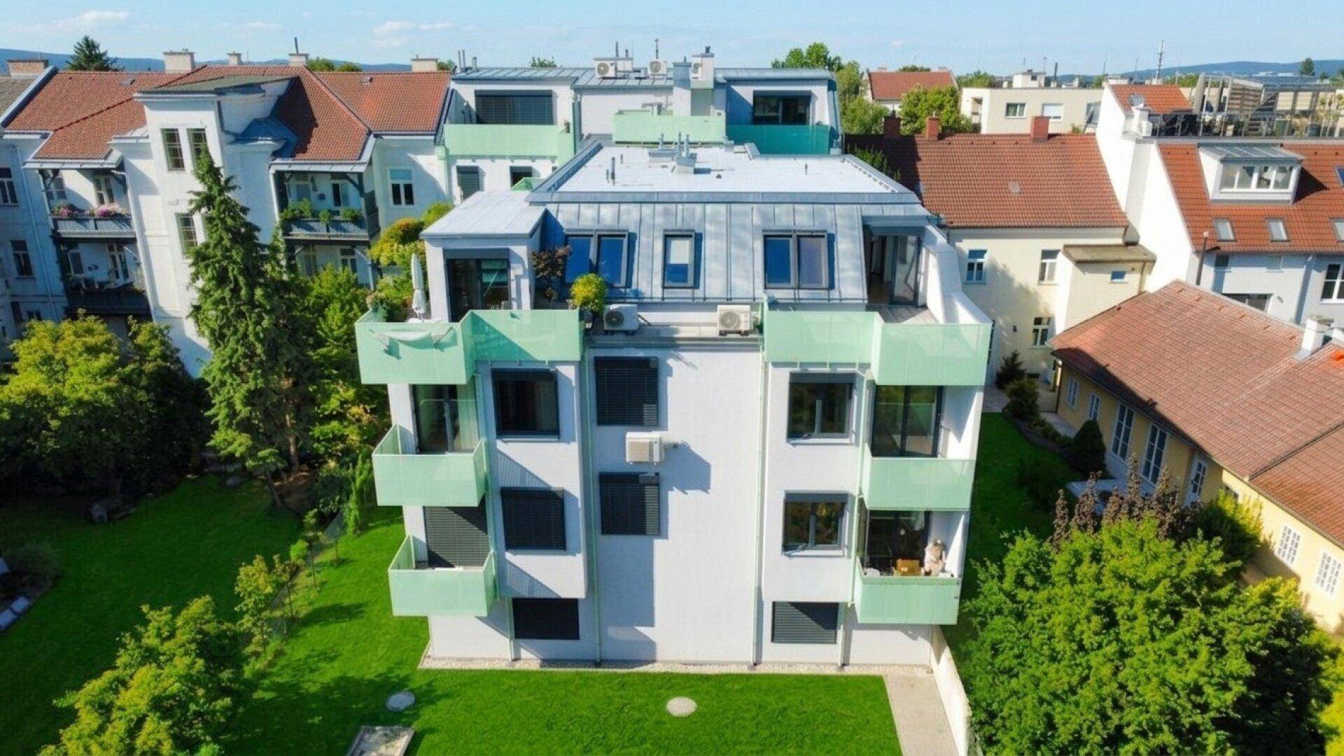 Luftaufnahme eines modernen Mehrfamilienhauses mit grünen Balkonen und gepflegter Rasenfläche.