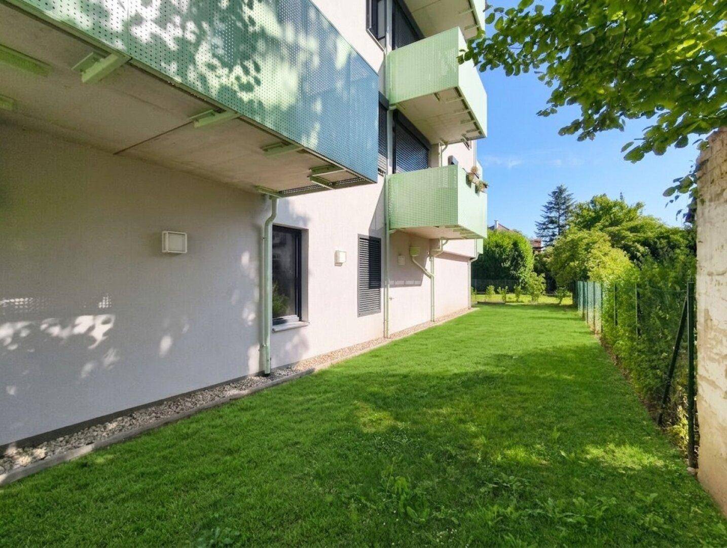 Gepflegter Rasenbereich entlang der Gebäudeseite mit grünen Balkonen.
