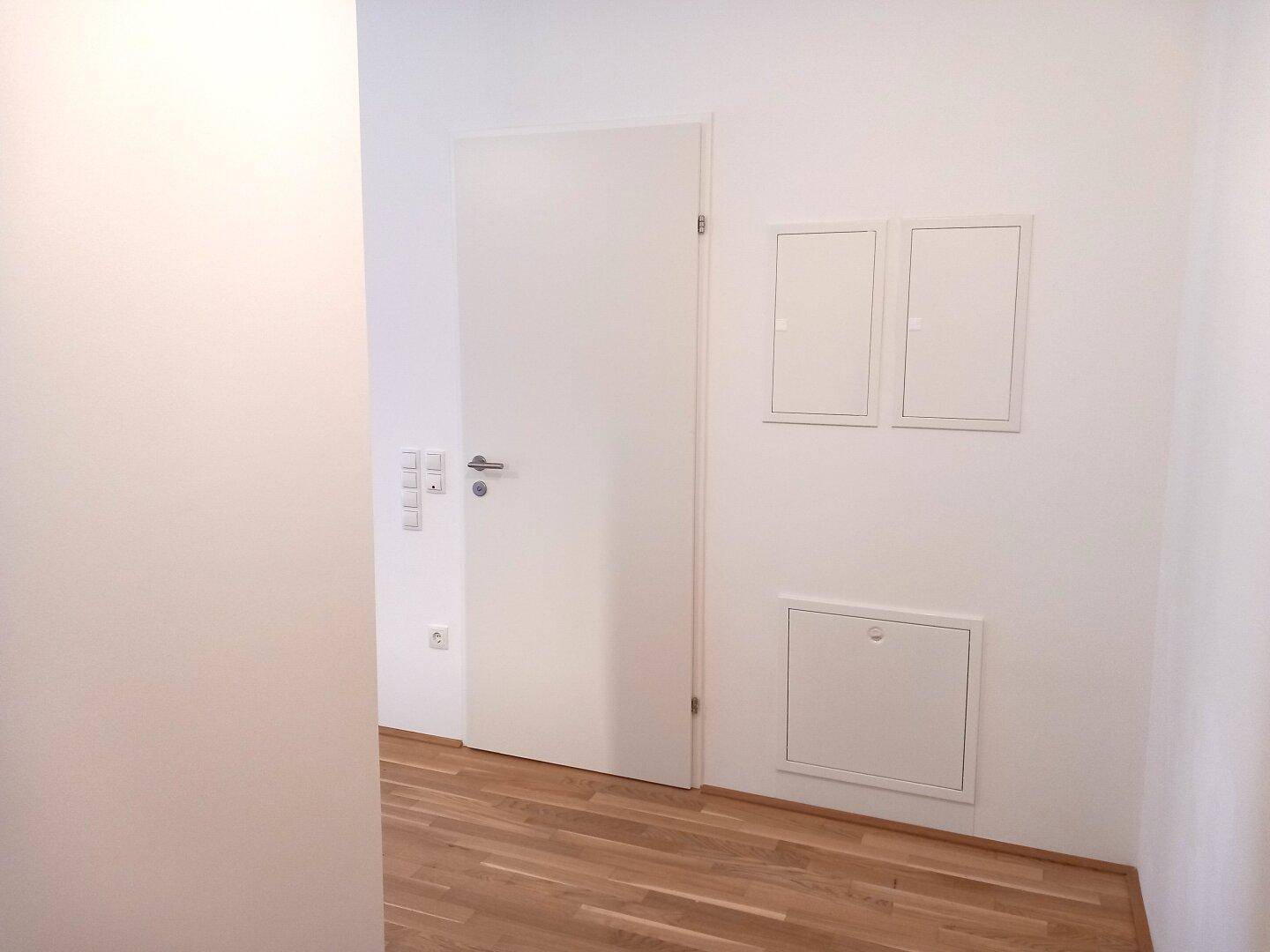 Heller Flur mit Parkettboden und Zugang zu den Zimmern, mit praktischen Wandpaneelen.
