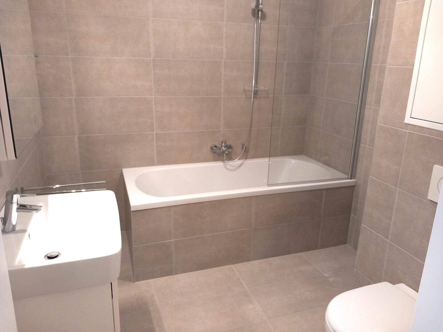 Zeitgemäßes Badezimmer mit Badewanne und Duschabtrennung, Waschbecken und Wand-WC.