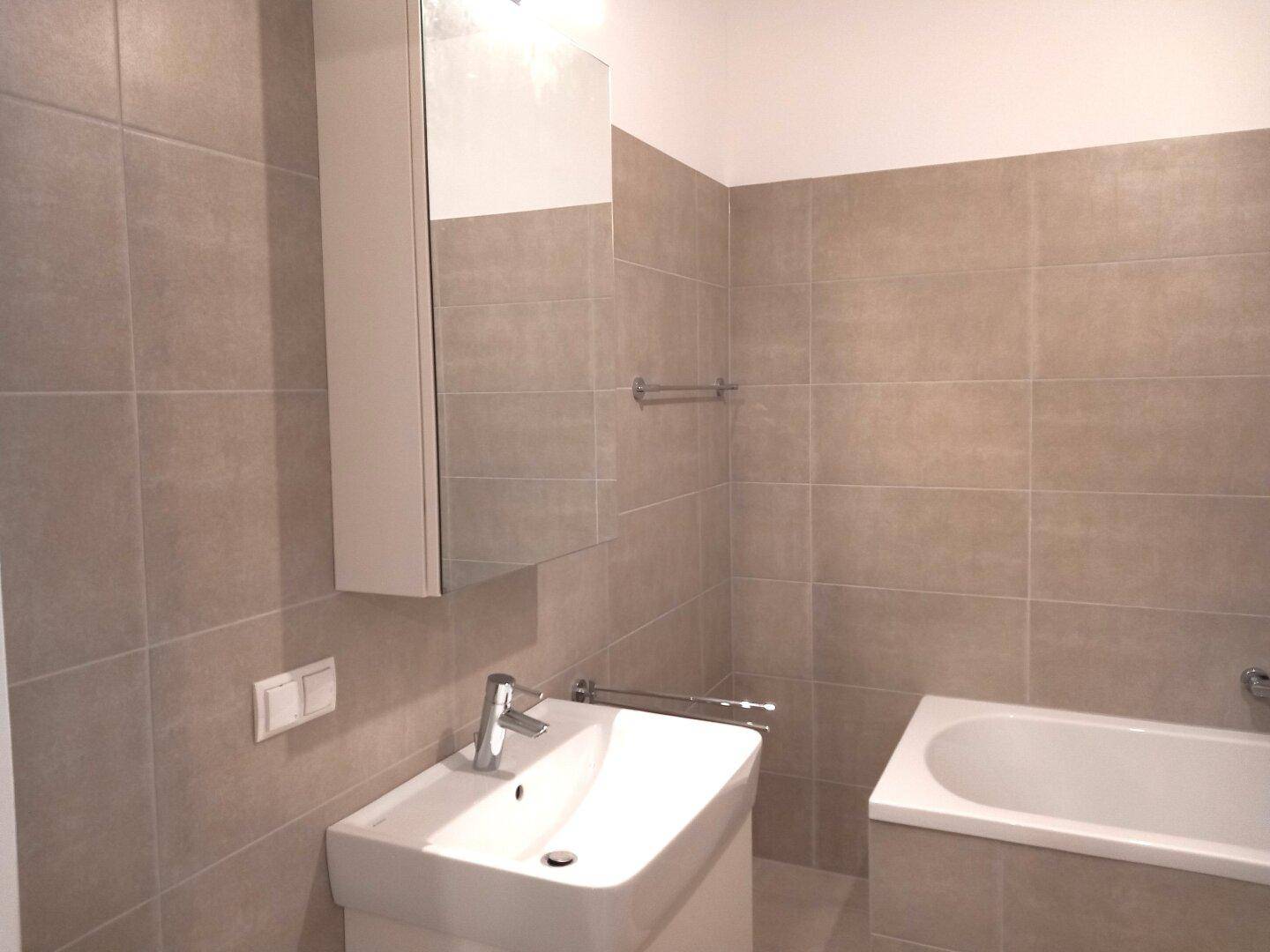 Modernes Badezimmer mit Badewanne, Waschbecken und Spiegelschrank, komplett gefliest.