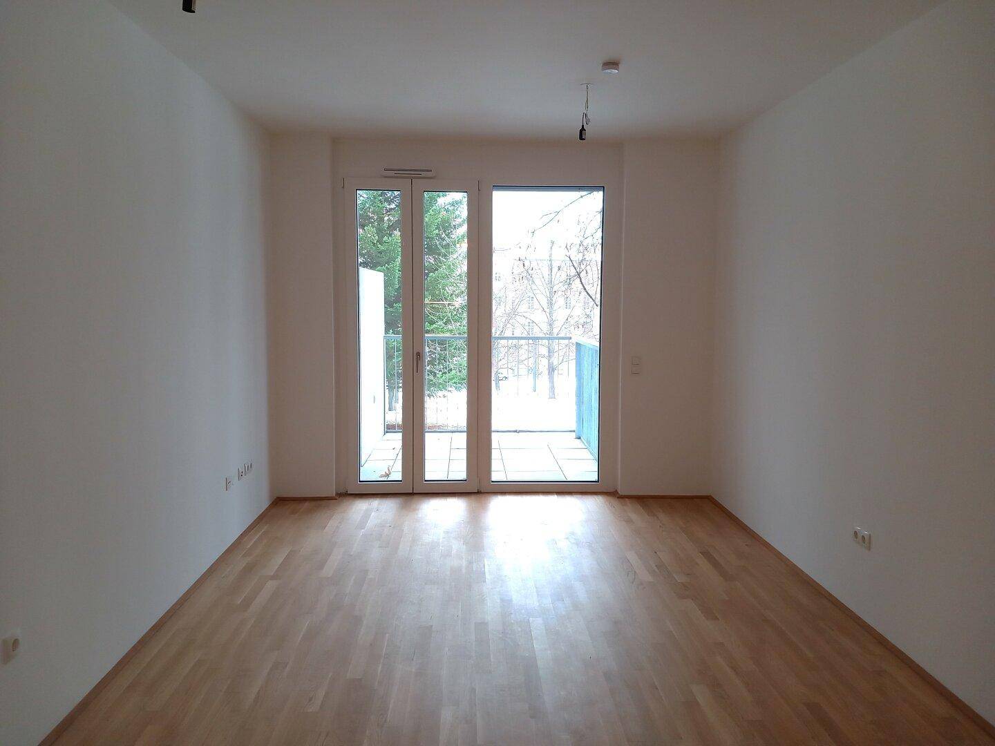Geräumiges, helles Wohnzimmer mit Parkettboden und großem Fenster, das viel Tageslicht hereinlässt.