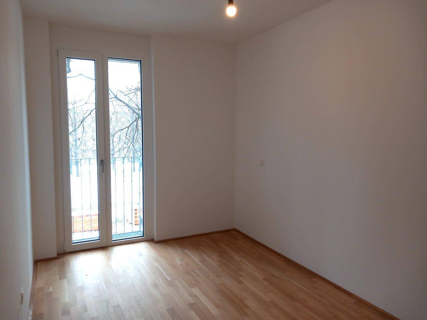 Helles Schlafzimmer mit Parkettboden und Zugang zu einem französischen Balkon, ideal für Ruhe.