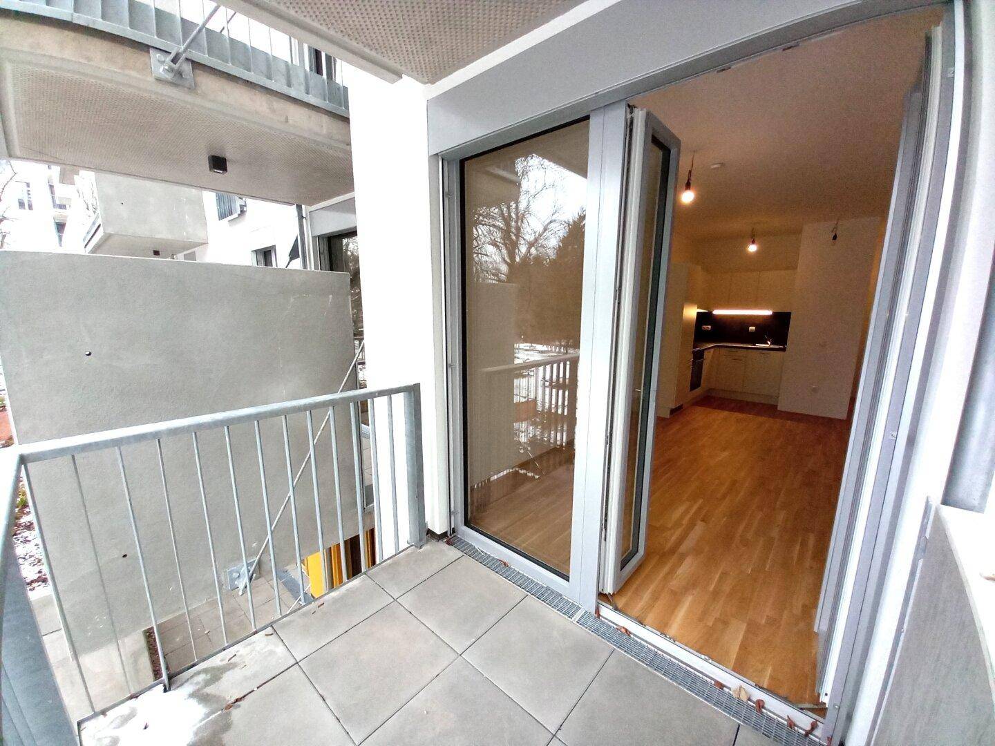 Geräumiger Balkon mit Fliesenboden und Blick in den Innenhof, direkt vom Wohnbereich zugänglich.