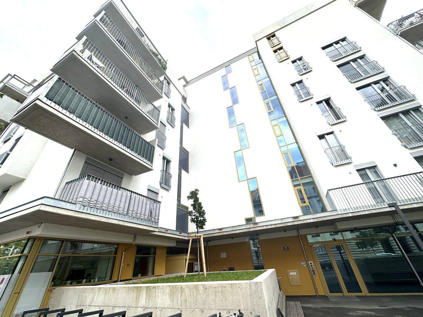 Moderne Wohnanlage mit Balkonen und farbigen Akzenten an der Fassade unter bewölktem Himmel.