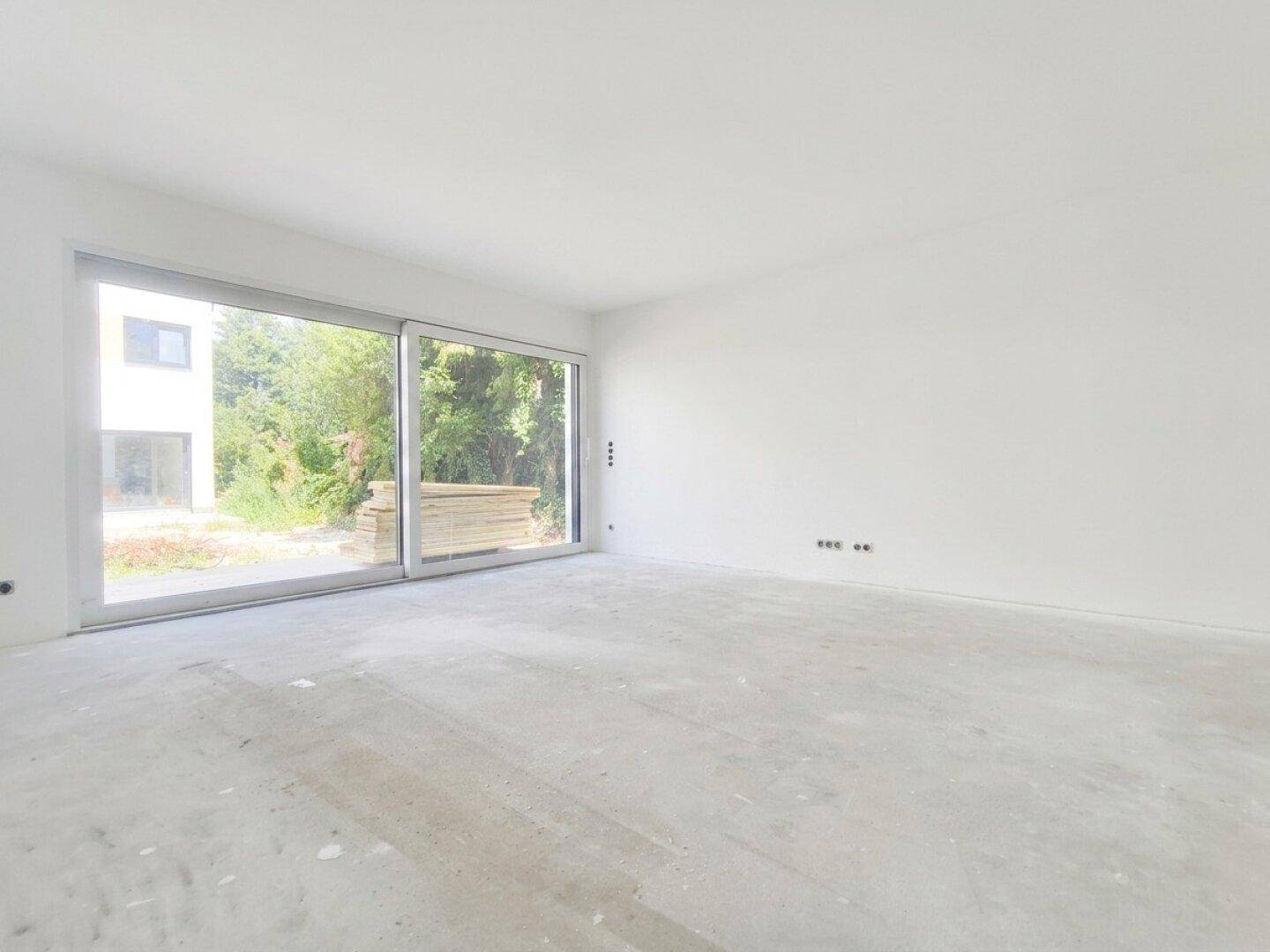 Geräumiger, unmöblierter Raum mit großen Fensterfronten und Blick ins Grüne.
