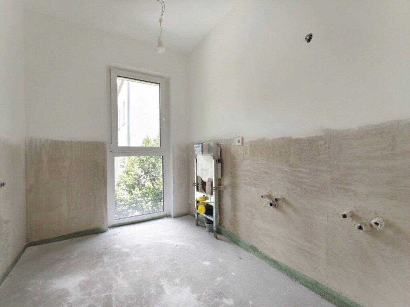 Unfertiges Badezimmer mit Rohinstallationen und einem großen Fenster, bereit für den Ausbau.