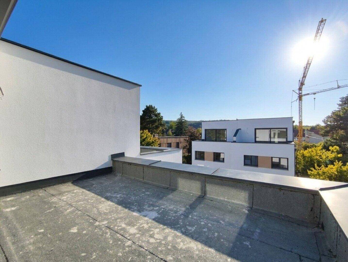 Sonnige Dachterrasse mit Blick auf die umliegenden Gebäude und einen Baukran am Horizont.