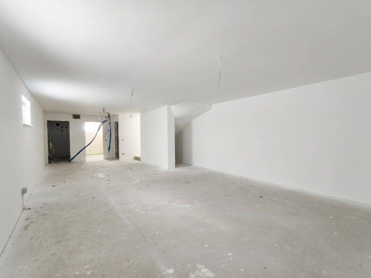 Großer, unmöblierter Kellerraum mit Rohbetonboden und sichtbaren Installationen, bereit für den Ausbau.