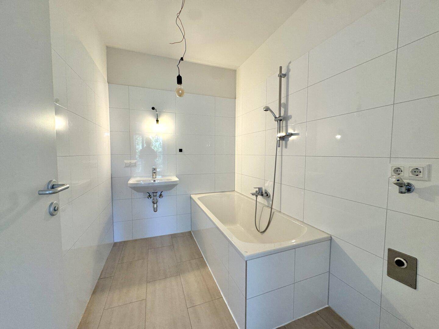 Helles Badezimmer mit weißen Fliesen, einer Badewanne und einem Waschbecken.
