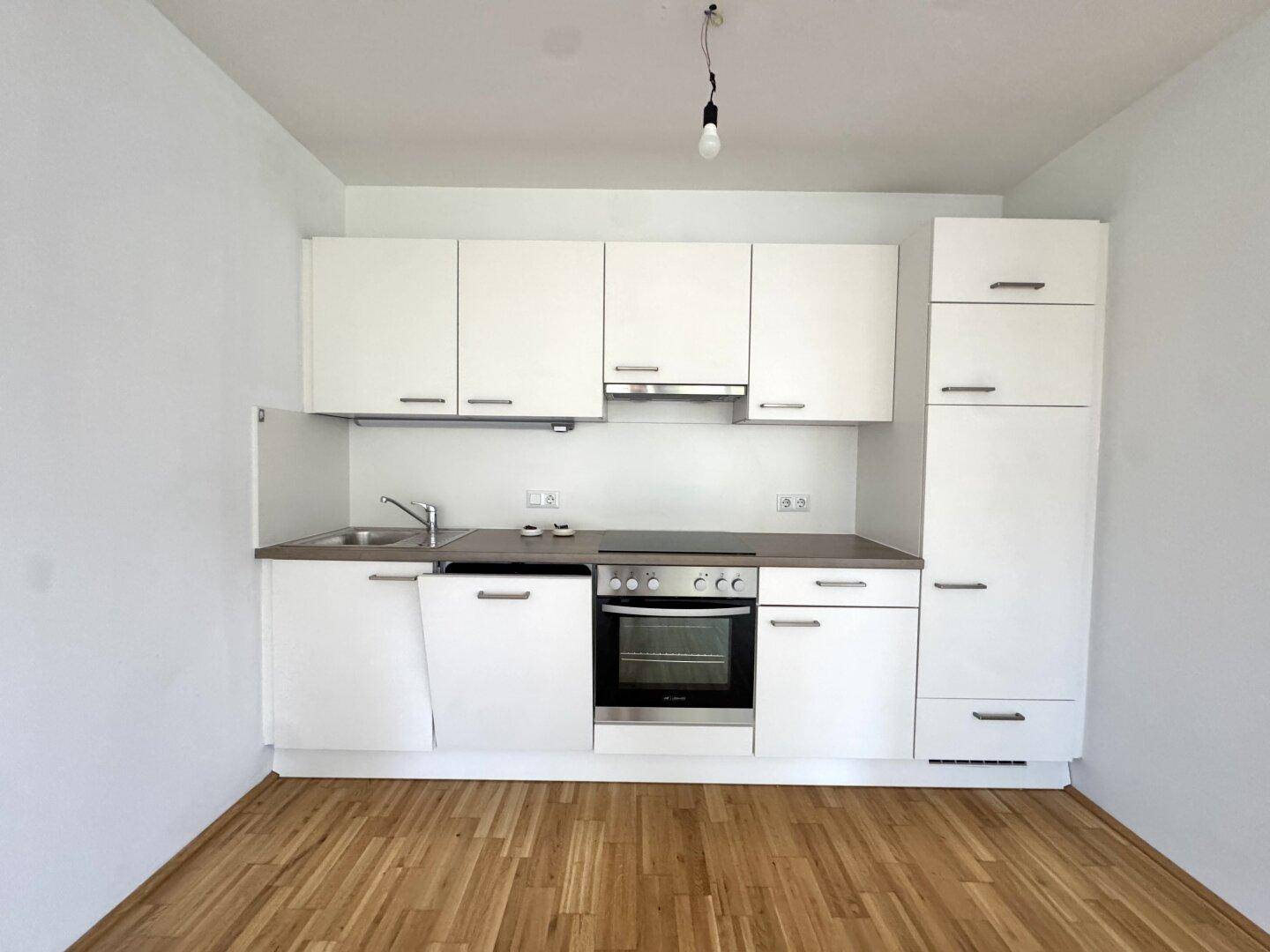 Moderne Küchenzeile mit weißen Schränken, integriertem Backofen und Spüle.