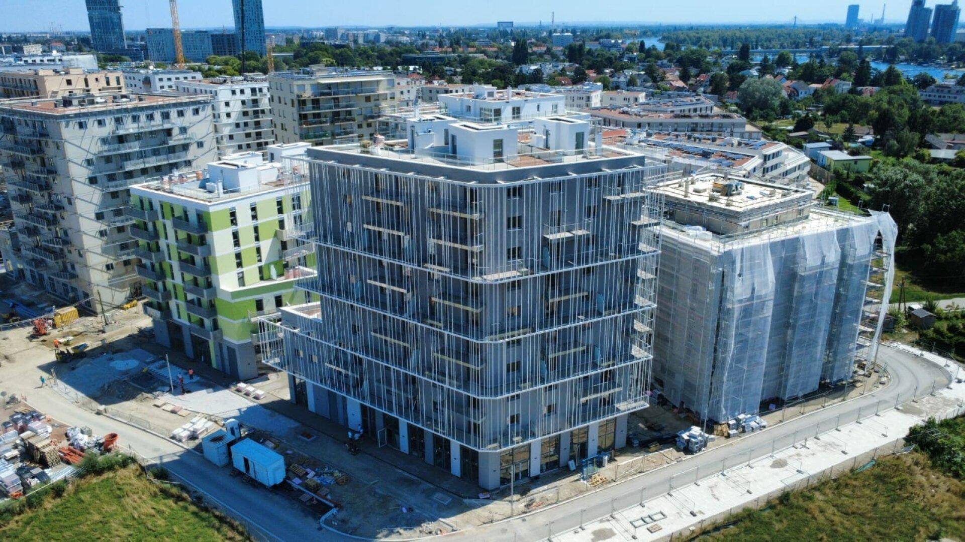 Luftaufnahme eines Neubaukomplexes mit modernen Fassaden und umliegenden Baustellenbereichen.