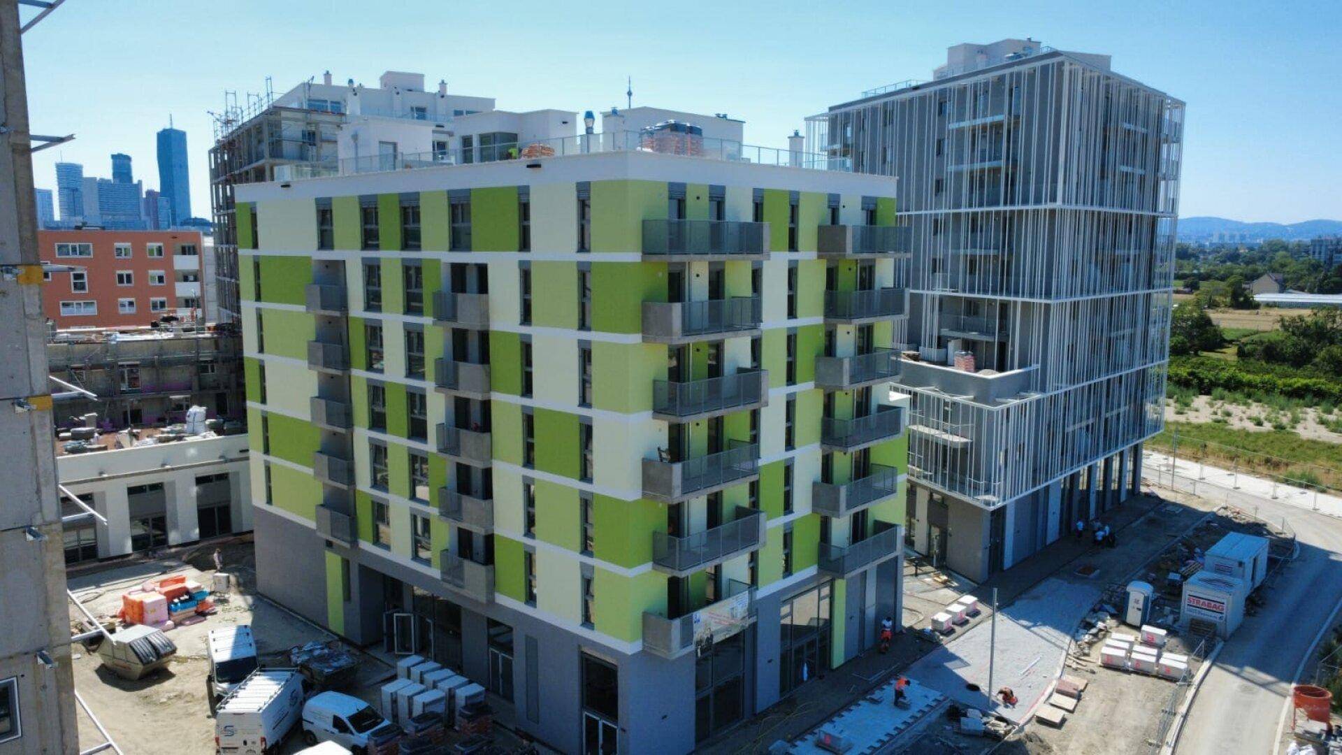 Nahaufnahme eines modernen Neubaus mit grüner und beiger Fassade sowie Balkonen.