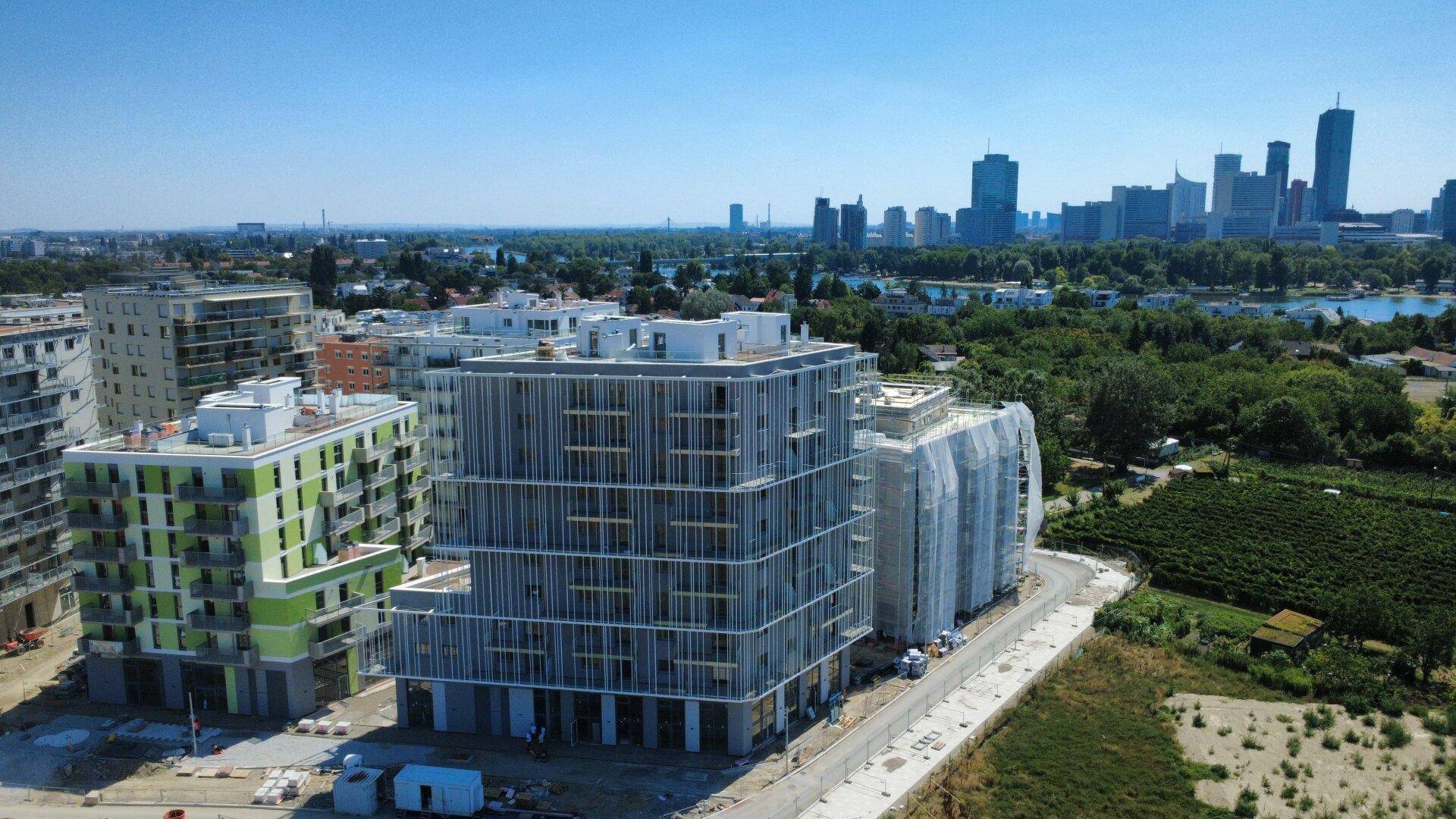 Luftaufnahme von Neubauten mit moderner Architektur und Blick auf die Wiener Skyline und die Donau.