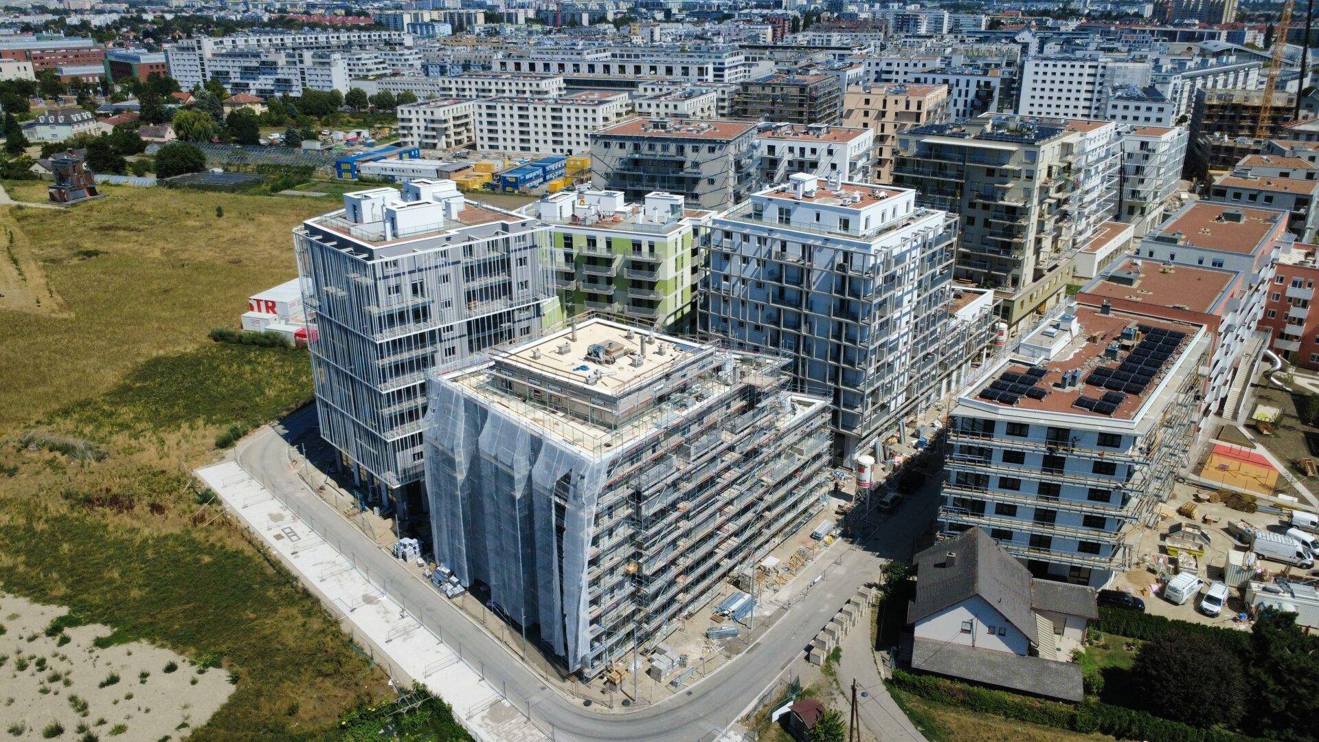 Weitläufige Neubausiedlung mit vielen Gebäuden und einem traditionellen Haus im Vordergrund.