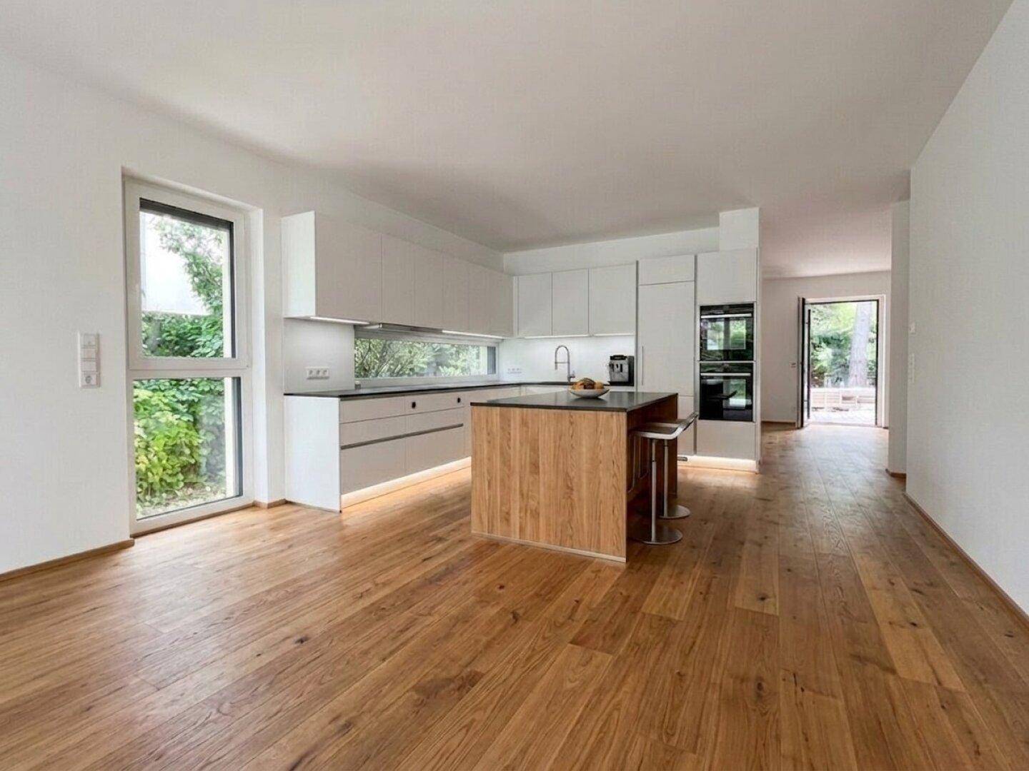 Offene, moderne Küche mit Kücheninsel, Holzboden und großen Fenstern zum Garten.