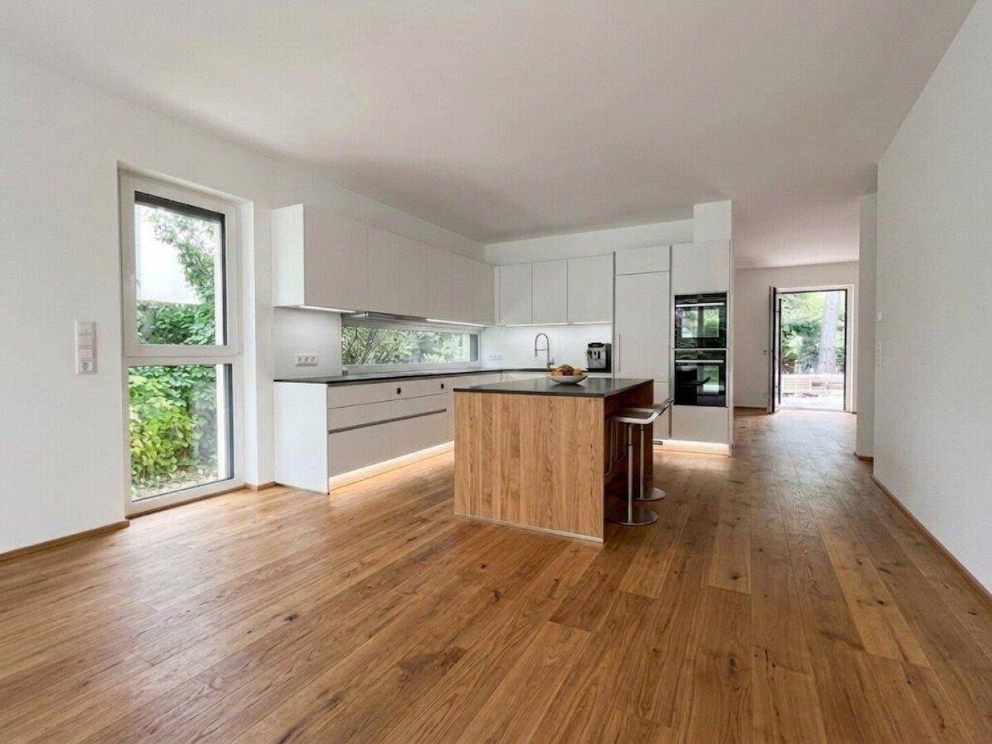 Helle, offene Küche mit moderner Kücheninsel aus Holz und integrierten Geräten, Blick ins Grüne.