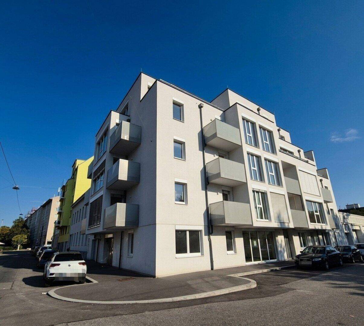 Eckansicht eines modernen Wohngebäudes mit Balkonen und heller Fassade unter klarem Himmel.