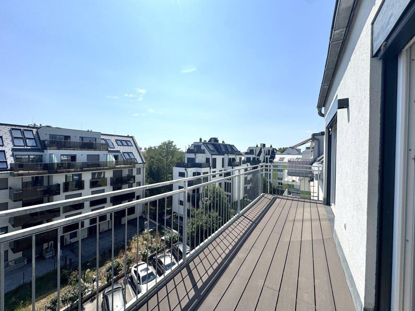 Geräumiger Balkon mit Holzboden und Metallgeländer, bietet Blick auf die Nachbarschaft und Parkplätze.