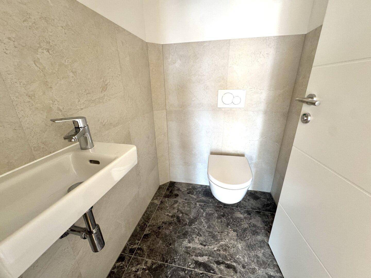 Kleines Gäste-WC mit wandhängendem WC und modernem Waschbecken, in hellen Fliesen gehalten.