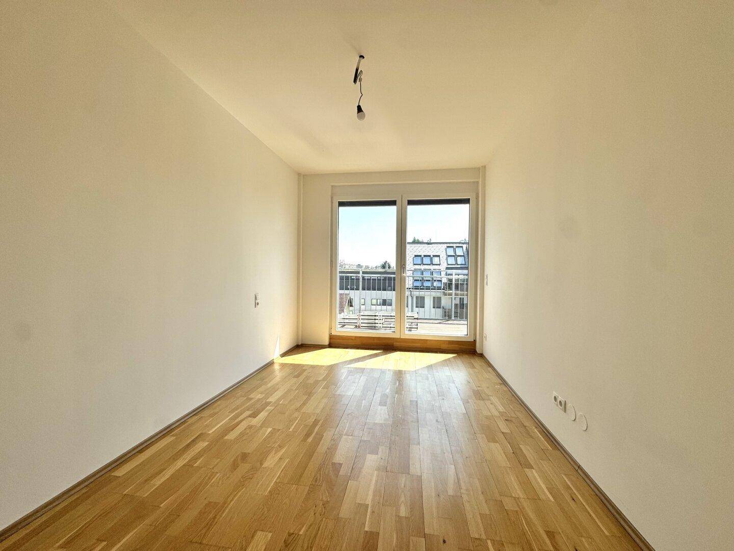 Helles Zimmer mit Holzboden und großen Fenstern, bietet viel Tageslicht und einen weiten Blick.