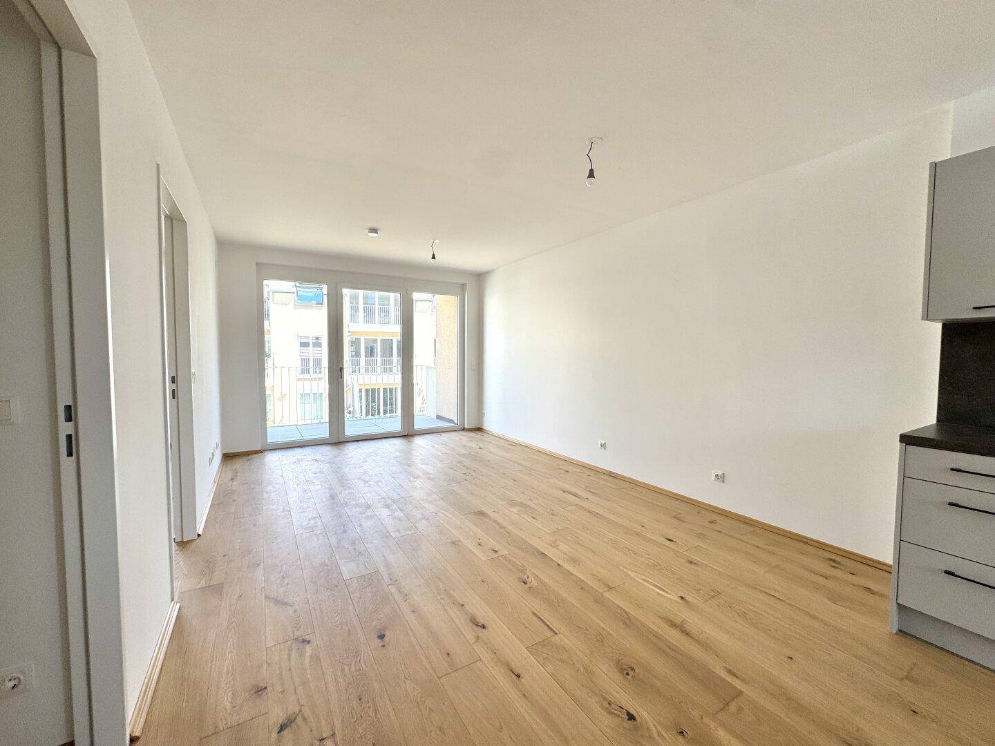Offener Wohnbereich mit integrierter Küche, Holzboden und direktem Zugang zum Balkon.