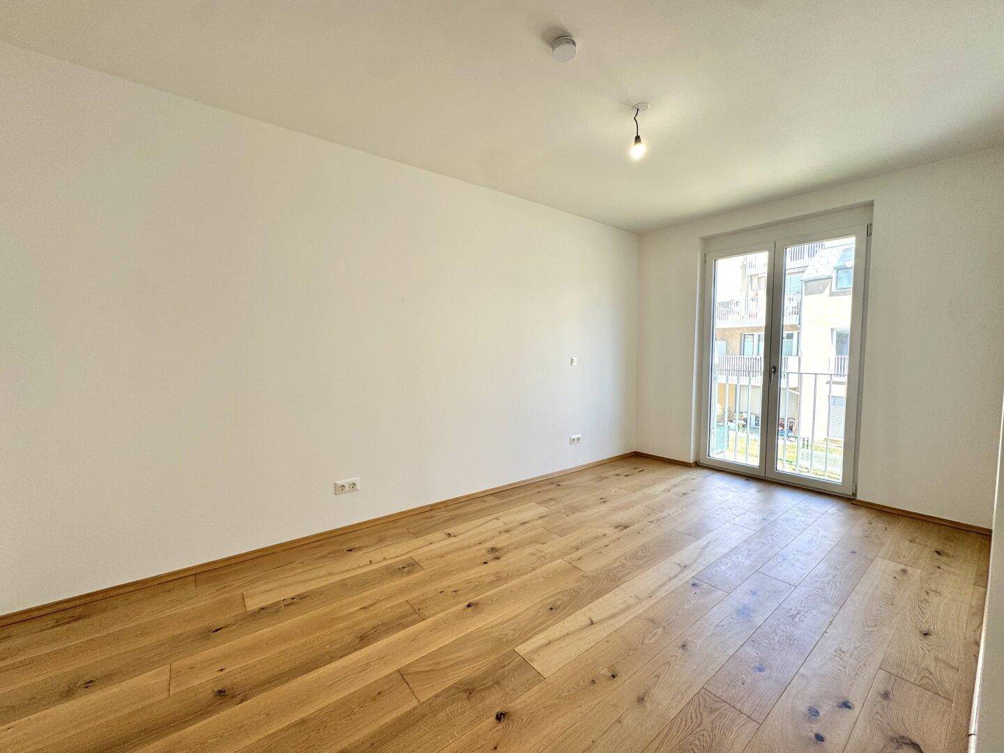 Geräumiger, heller Raum mit Holzboden und großem Fenster, ideal als Wohn- oder Schlafzimmer.
