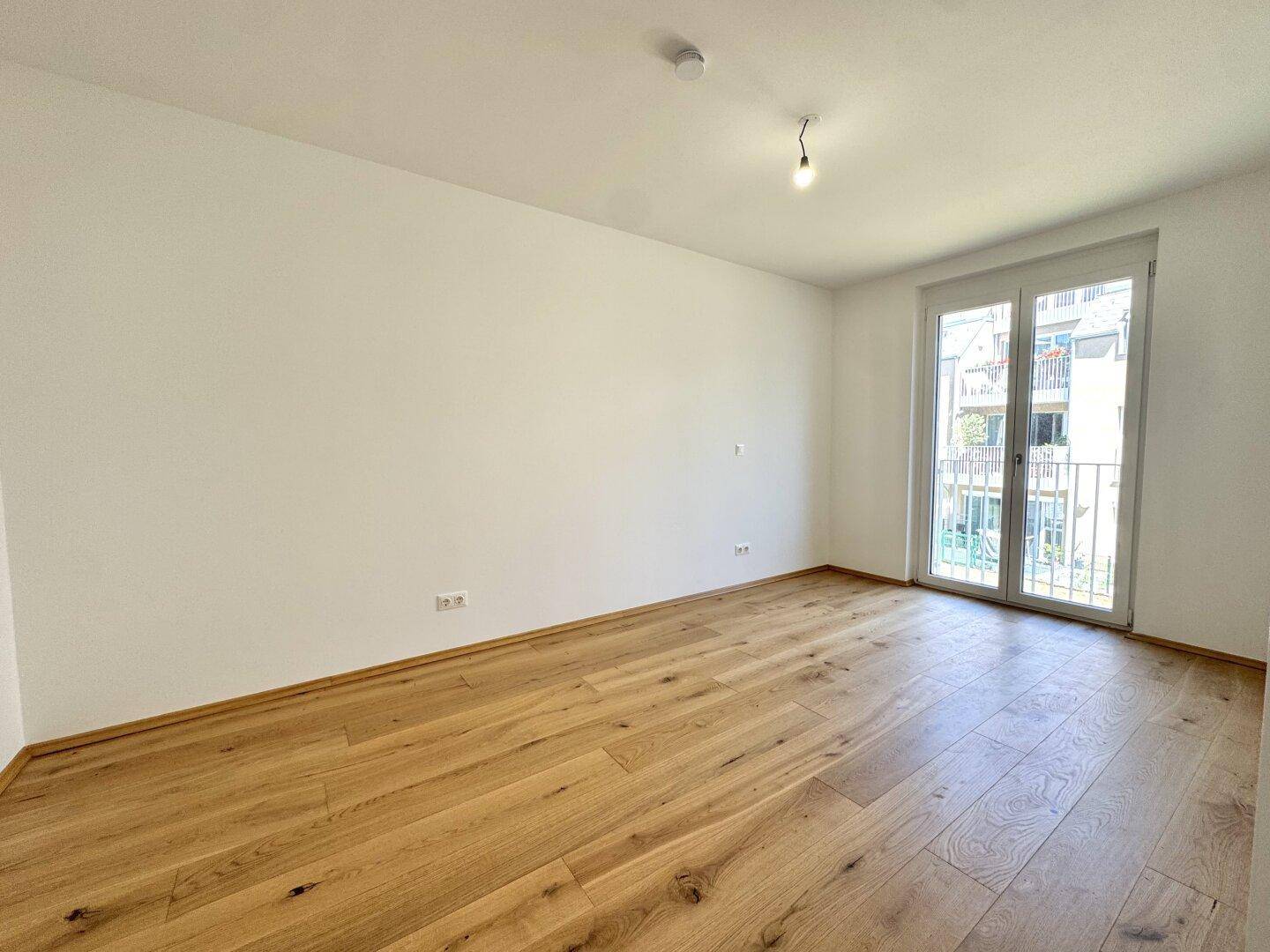 Leerer Raum mit Holzboden und großer Balkontür, ideal als Schlaf- oder Wohnzimmer.