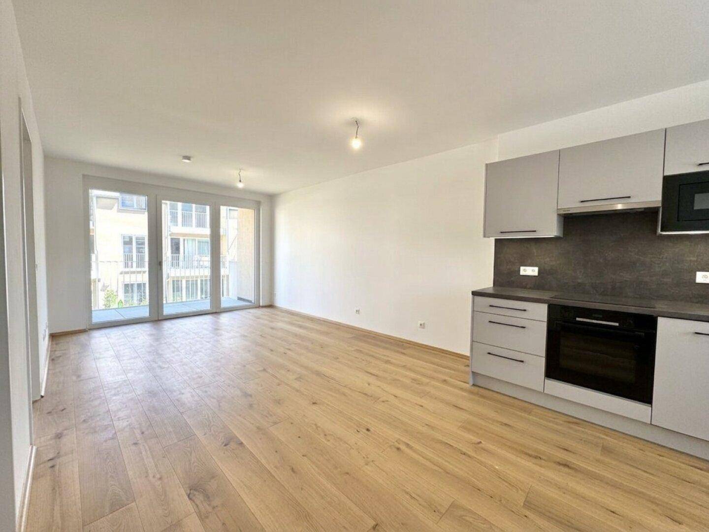 Heller offener Wohnbereich mit Holzboden und Zugang zu einem Balkon, angrenzend an die Küche.
