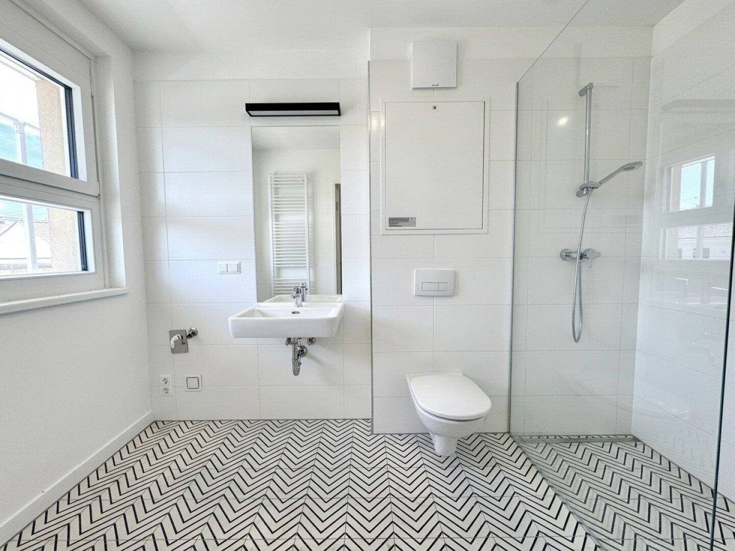Modernes Badezimmer mit weißen Fliesen, ebenerdiger Dusche, WC und Fenster.